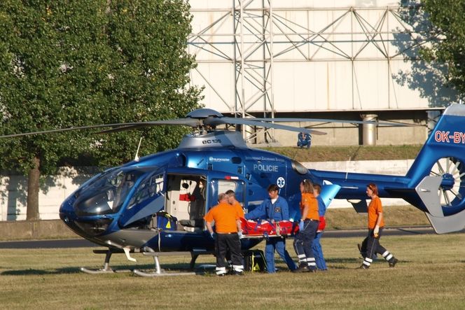 Kralupští Samaritáni přemísťují stabilizovaného pacienta na palubu záchranářského Eurocopteru, který s ním ihned odletí na heliport pražské FNKV. 