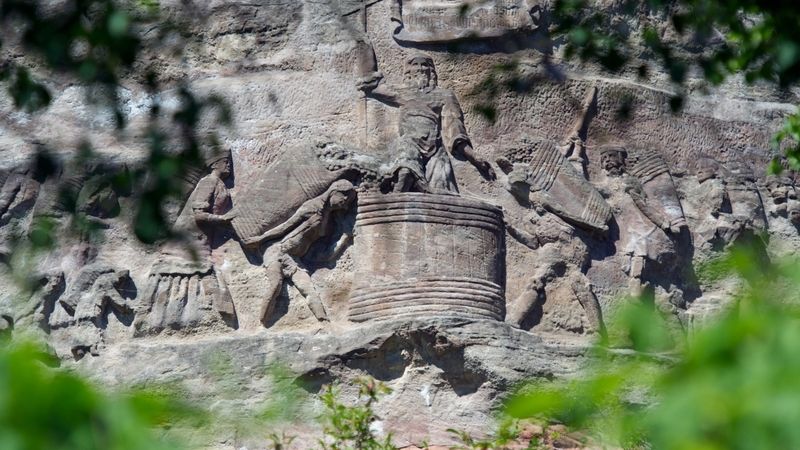 Neznámý autor do pískovcové stěny vytesal 12 reliéfů v nadživotní velikosti táhnoucích se v délce 150 metrů. 