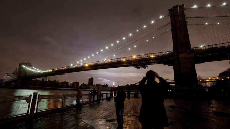 Lidé si fotografují Brooklynský most. Jako jeden z mála objektů v New Yorku je osvětlen.