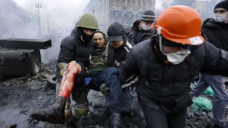 Demonstranti v Kyjevě odnášejí zraněného.