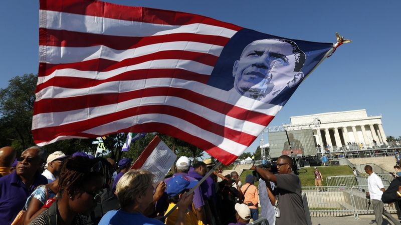 Jeden z účastníků pochodu drží v rukách vlajku s prvním černošským prezidentem USA Barackem Obamou.