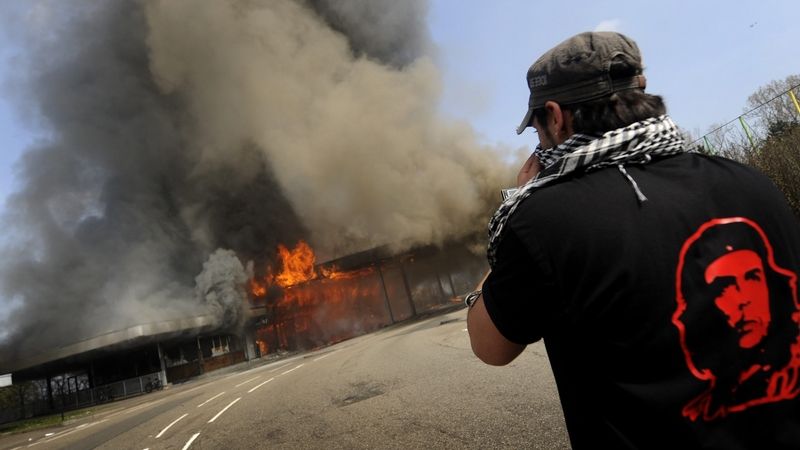 Demonstrant pozoruje hořící budovu pohraniční stráže. 