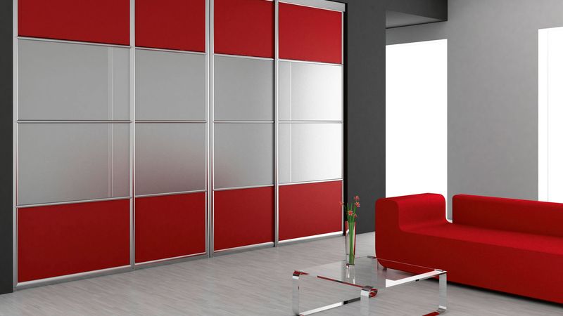 Výhodou skříně na míru je, že ji lze barevně sladit s ostatním vybavením interiéru. Výplň posuvných dveří v hliníkovém rámu tvoří kombinace šedo-červeného lamina. 