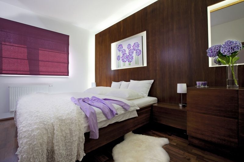 Nábytek v ložnici je zhotovený na míru. Klasické čelo postele nahradila dřevem obložená stěna s integrovaným zrcadlem. Zajímavé je i po obvodu nainstalované osvětlení. 
