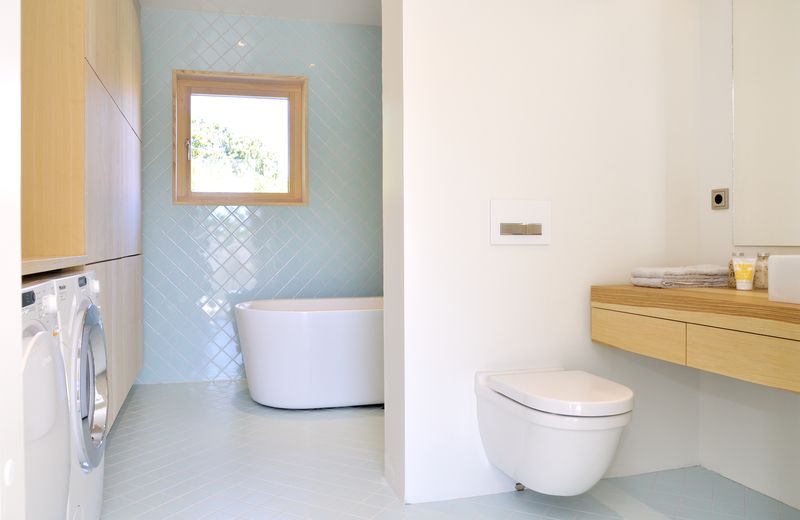 Koupelna je obložena čtvercovými dlaždicemi bledě modré barvy orientovanými na koso.