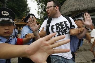 Policisté brání natáčení demonstranta v tričku Free Tibet.