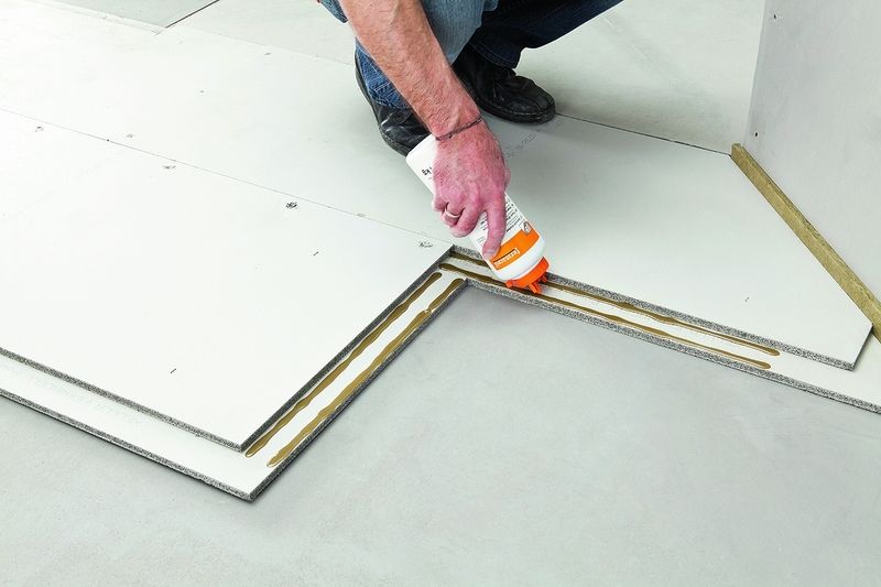 Lepení suchých podlahových prvků Fermacell – na polodrážku naneseme podlahové lepidlo (dva proužky 5 mm silné) a oba prvky se na sraz sesadí.