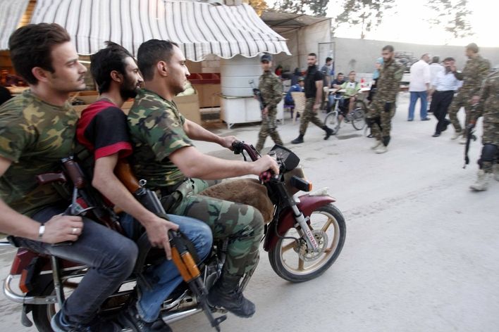 Šíitští bojovníci z Iráku se svými zbraněmi jedou na motocyklu.