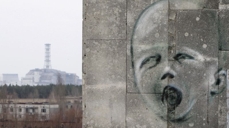 Graffiti na zdi v liduprázdném městě Pripjať. V pozadí je zapečetěný havarovaný čtvrtý blok elektrárny Černobyl.