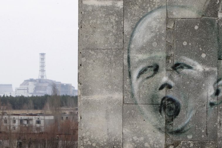 Graffiti na zdi v liduprázdném městě Pripjať. Na pozadí zapečetěný havarovaný čtvrtý blok elektrárny Černobyl.
