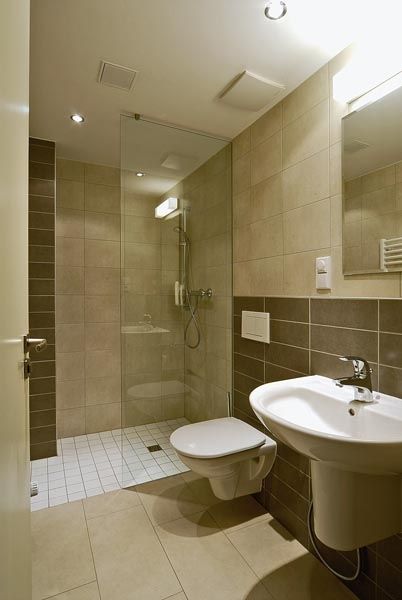 Koupelna v přízemí nemá okno, proto je obložena obkladem ve světlých matných odstínech a sprchový kout oddělen silnostěnným sklem. Horizontální linie obkladu opticky zvětšuje nevelkou místnost.  