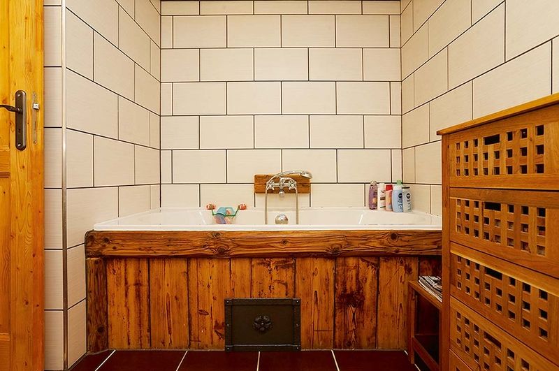 V koupelně jsou dřevem obložené vana, baterie. 