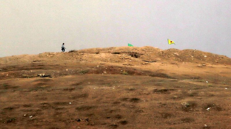 Milicionář YPG na návrší u kurdské vlajky. 