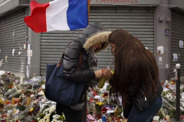 Ženy zapalují svíčku na místě jednoho z útoků v Paříži.