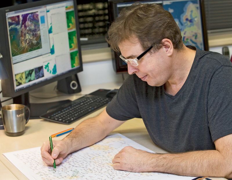 Letecký meteorolog Petr Dvořák analyzuje mapu, přičemž každý jev maluje jinou barvou. Kupříkladu oblasti trvalých srážek zeleně, mlhy zase žlutě.