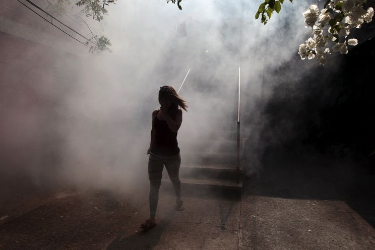 Žena v Salvadoru odchází z domu, kde zdravotníci vykuřují moskyty.