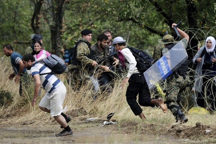 Migranti překonávající zátarasy na hranicích mezi Řeckem a Makedonií.