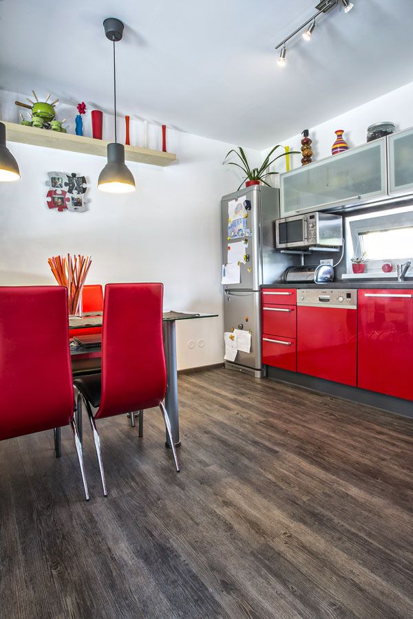 V kuchyni najdete i jídelní sekci se stolem a židlemi. Všimněte si hezkého barevného sladění židlí a spodních skříněk kuchyňské linky – veselý odstín červené barvy vnáší do interiéru dynamiku, pohyb a teplo.