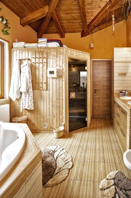 V prostorné koupelně obložené keramikou s motivem dřevěné textury se našlo místo i pro saunu. Z vany se nabízí příjemný pohled na dřevěné trámy a prkenný záklop střechy.