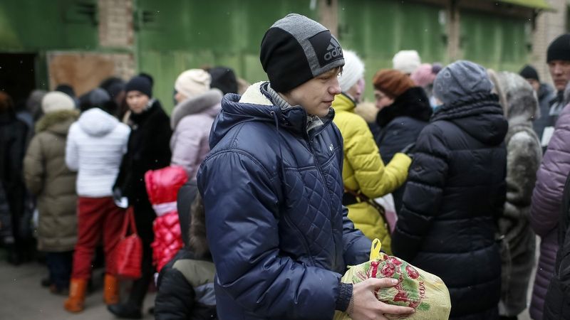 Evakuovaná Ukrajinka si odnáší potravinovou pomoc, další na ni čekají.