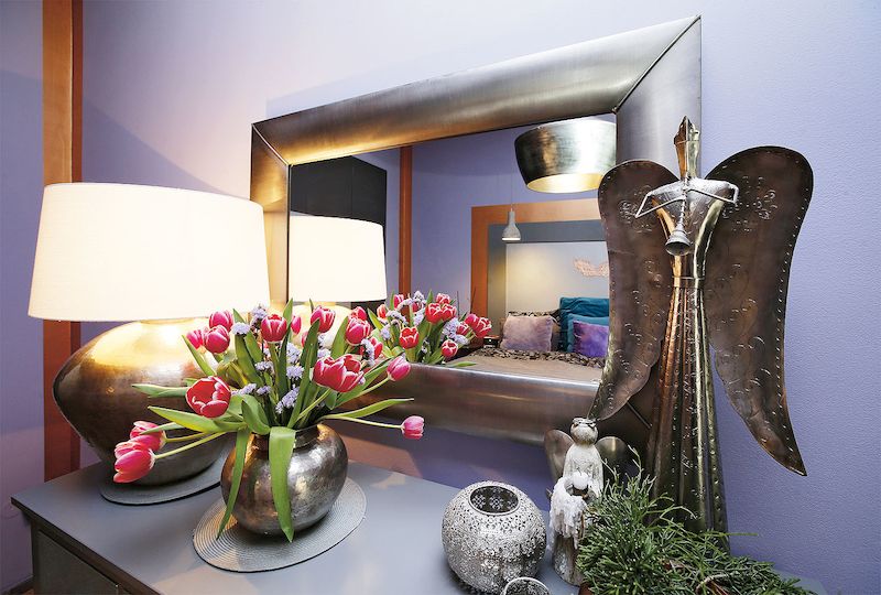 V ložnici je zrcadlo vsazené do stejného rámu jako fotografie orchideje v obývacím pokoji. Byt má jednotnou linku: spojuje ho fialová výmalba, květiny, lampy a kovové dekorace.