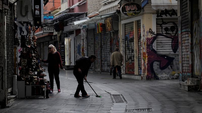 Muž uklízí časně ráno před obchodem v Aténách