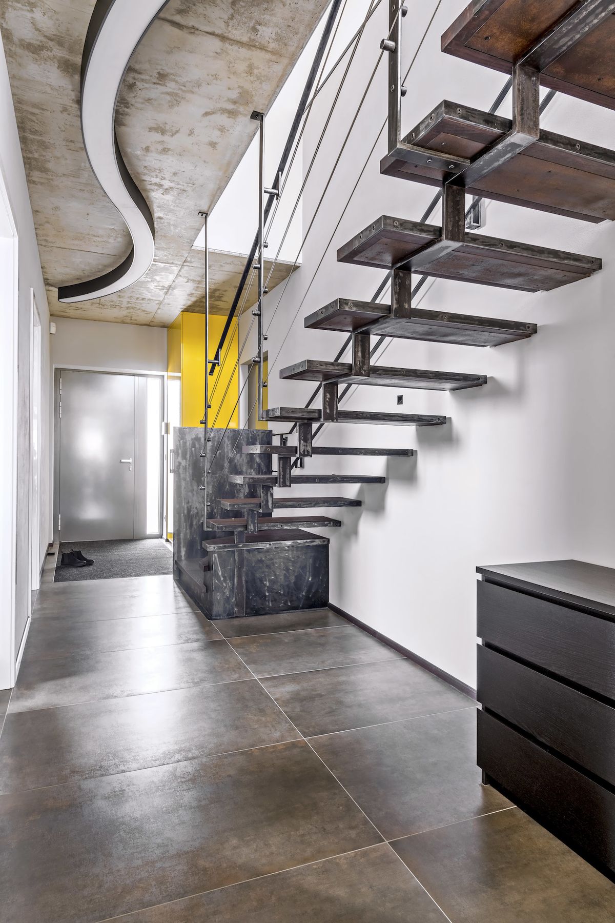 Nápadný akcent chodby s industriálně laděným schodištěm, vyrobeným místním uměleckým kovářem, tvoří kontrastní žlutá skříň (Hanák nábytek) lakovaná do vysokého lesku.