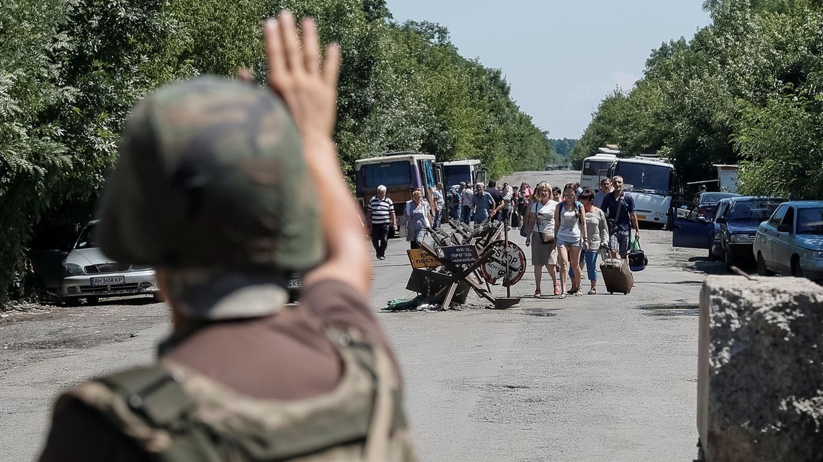 Ukrajinský voják dává pokyn lidem pohybujícím se poblíž kontrolního stanoviště ve městě Majorsk.