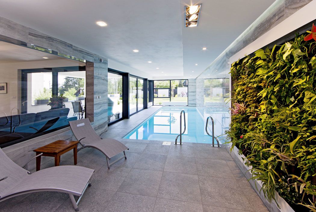 Bazén s prosklenými stěnami působí jako pokračování zahrady v interiéru. Kvetoucí zelená stěna sem přináší svěžest a živé barvy přírody.