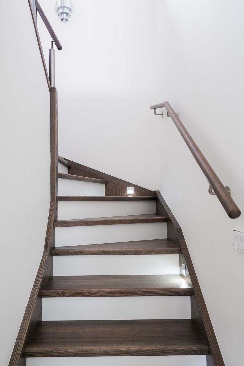 Elegantní kombinace bílých stěn a tmavohnědých dřevěných stupňů schodišti vysloveně sluší.