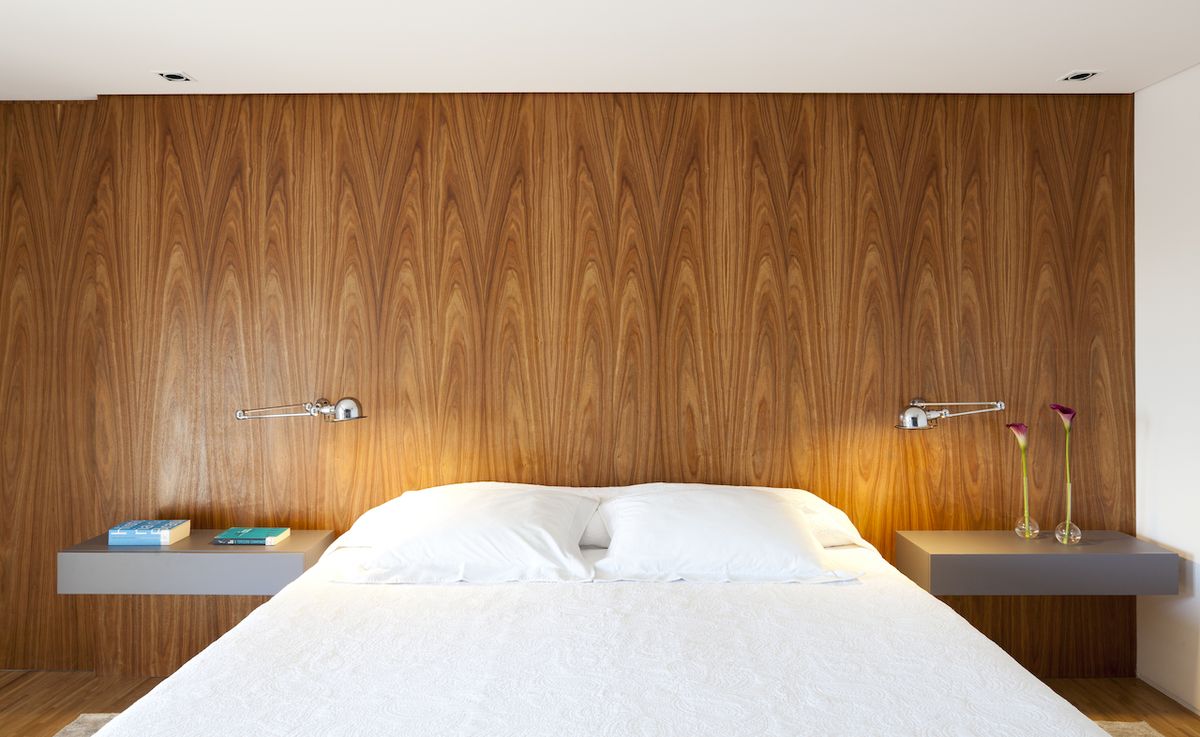 Minimalisticky řešené noční stolky jsou opět protipólem k živěji působícímu dřevěnému panelu za postelí.