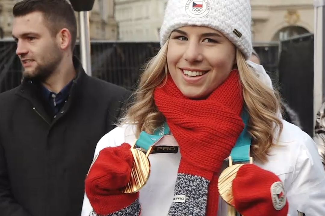 Ester Ledecká se svými medailemi na Staroměstském náměstí, kde lidé vítají olympioniky.