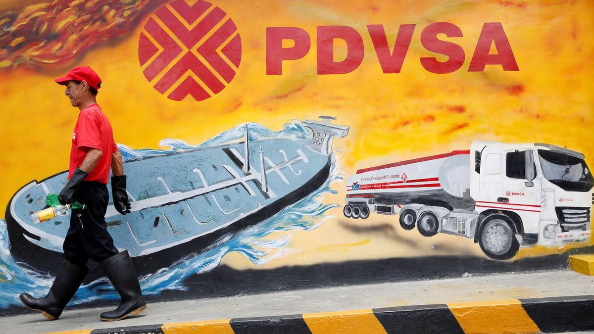 Zaměstnanec čerpací stanice v Caracasu před nástěnnou malbou s logem státní ropné firmy PDVSA.
