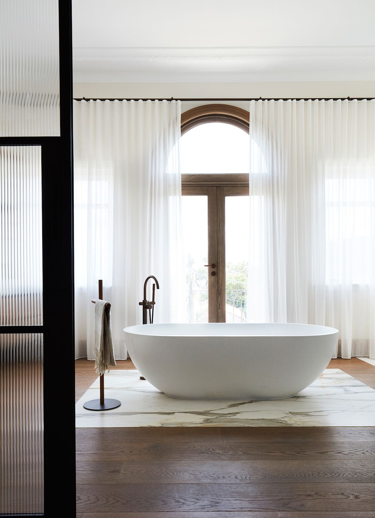 Intimní atmosféru koupelny u hlavní ložnice podporují dlouhé bílé závěsy, eleganci jako připomínku starých časů pak mosazná podlahová baterie vedle solitérní vany.