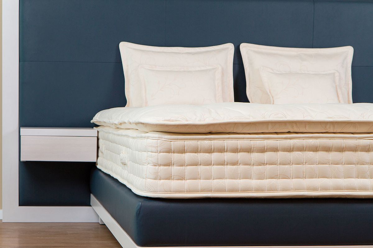 Luxusní kontinentální postel Carina se skládá z divanu, matrace a povrchové matrace, kterou regulujeme výšku lůžka. Je ručně vyrobena z ušlechtilého bílého masivu, doplněného tmavomodrou kůží a ručně vyrobenou přírodní matrací.