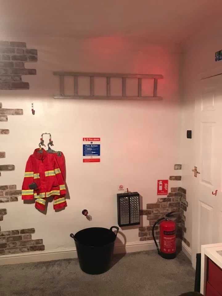 Na zdi nechybí požárnický oblek a žebřík, v rohu pokoje pak nezbytný hasičský přístroj.