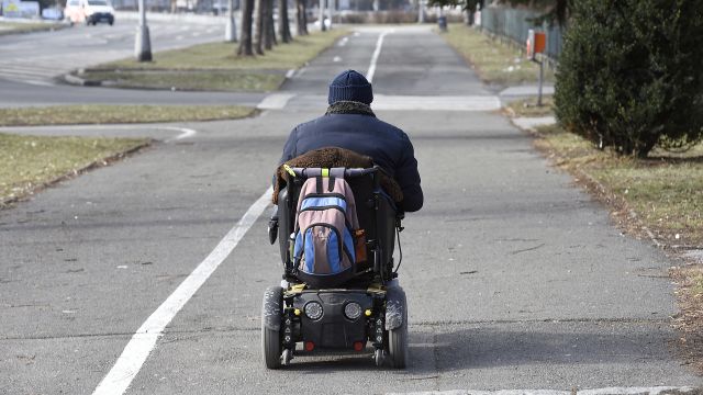 Invalida jedoucí po chodníku na elektrickém invalidním vozíku.