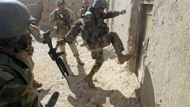 Afghánský voják sledovaný americkými vykopává dveře od domu v ulicích města Mardžáh.