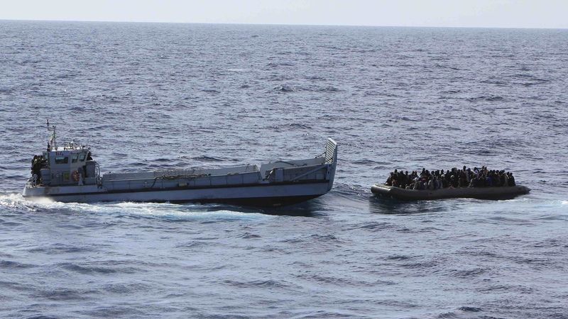 Migranti v gumovém člunu, které naložila výsadková loď italského námořnictva San Marco (vlevo) 
