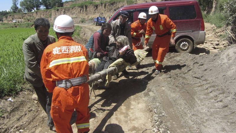 Hasiči pomáhají odnášet ženu zraněnou při zemětřesení v provincii Kan-su na severozápadě Číny.