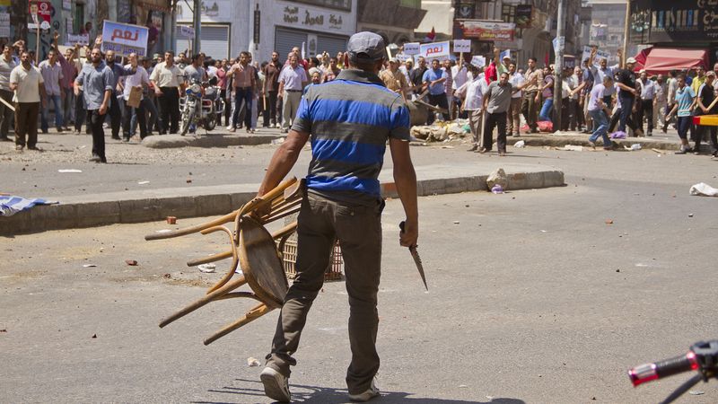 Vládní oponent s židlí a nožem v rukou stojí proti davu příznivců prezidenta Mursího.