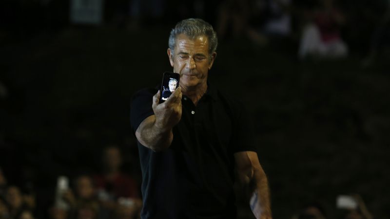 Mel Gibson drží v ruce mobil se svým portrétem.