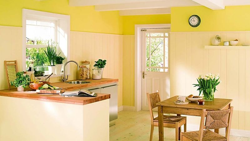 Kuchyň na venkově v barevné kombinaci: dřevěný strop čistě bílý, stěny krémový obklad a nad ním zářivě žlutá barva, která probudí organismus a zdrží léto v bytě i přes chladné měsíce. 