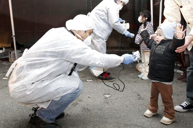 Kontrolor v ochranném obleku zjišťuje případnou radiaci u chlapce evakuovaného z okolí jaderné elektrárny Fukušima.