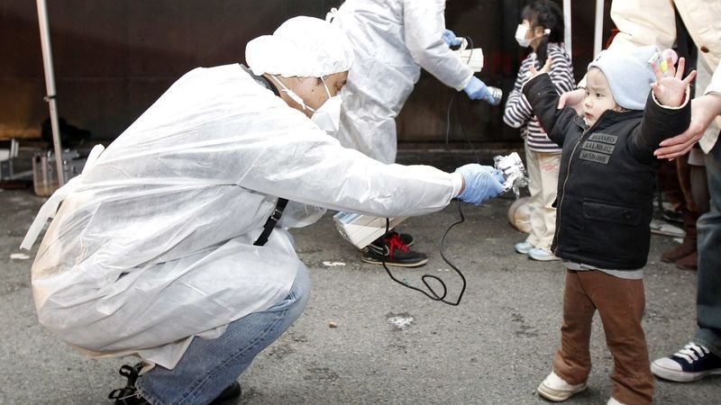 Kontrolor v ochranném obleku zjišťuje případnou radiaci u chlapce evakuovaného z okolí jaderné elektrárny Fukušima.