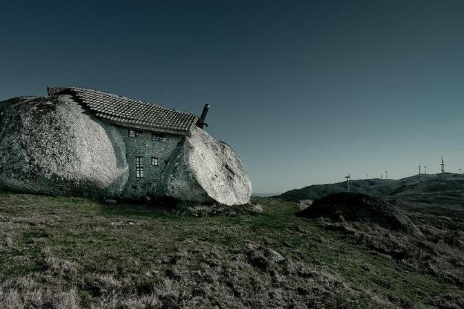 Kamenná domek stojí na pláni, v dálce jsou vidět větrné elektrárny.