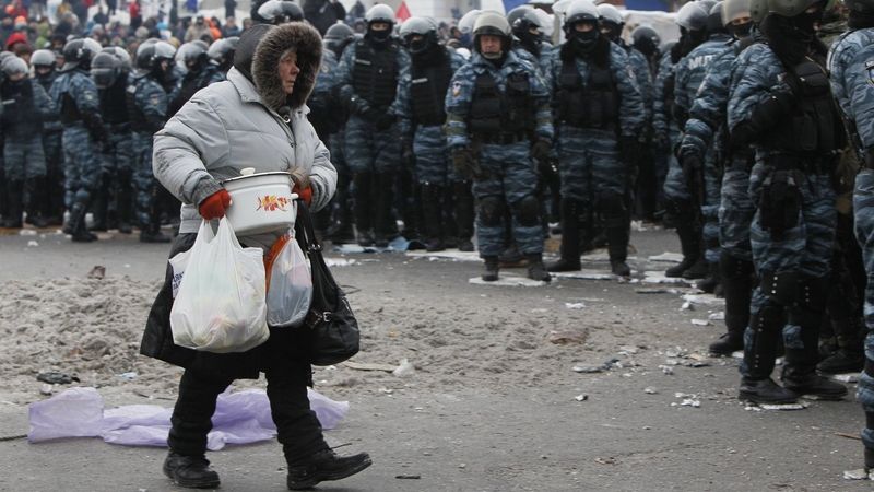 Ukrajinka nese jídlo demonstrantům podél policejního kordonu Berkutu.