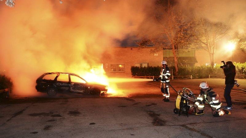 Hasiči na stockholmském předměstí Kista hasí zapálený vůz.