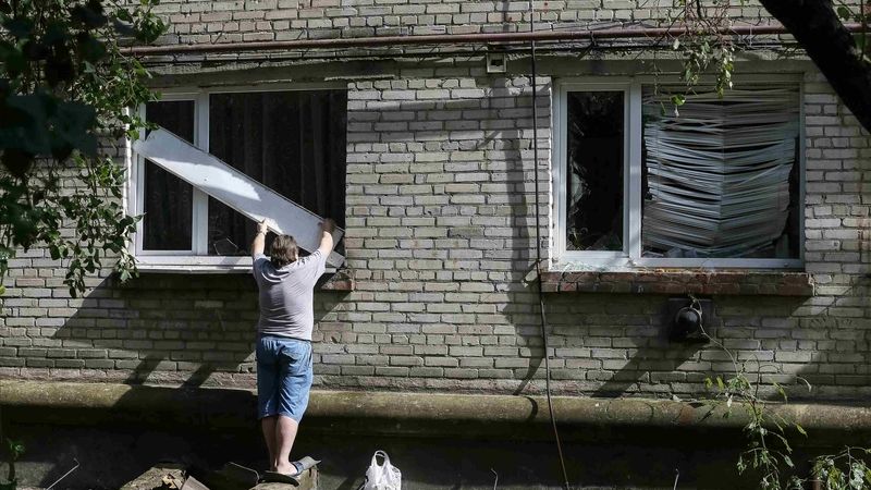 Muž provizorně zakrývá okno zničené palbou v domě ve Slavjansku.  