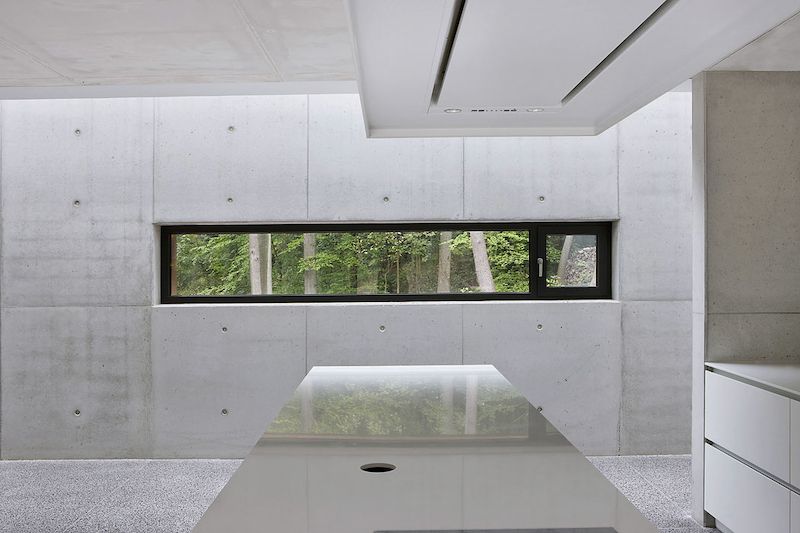 Interiér v tlumených šedých barvách dává vyniknout zeleni za okny. Na fotografii je kombinace pevného a otevíravého zasklení.